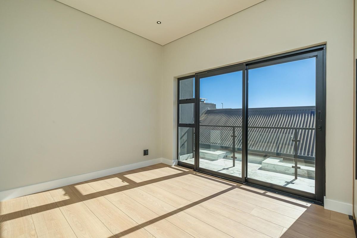 A bright, empty bedroom featuring modern laminate flooring, recessed lighting, and large sliding glass doors that open onto a private balcony.