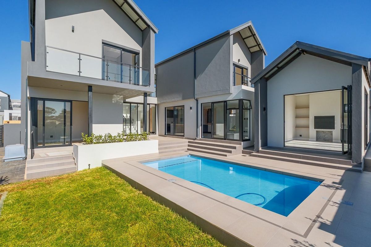 Modern multi-level home exterior featuring a swimming pool, tiled patio area, glass balcony, and seamless indoor-outdoor flow through large sliding doors.