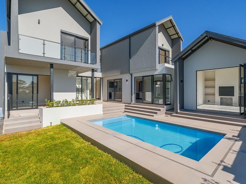 Modern multi-level home exterior featuring a swimming pool, tiled patio area, glass balcony, and seamless indoor-outdoor flow through large sliding doors.
