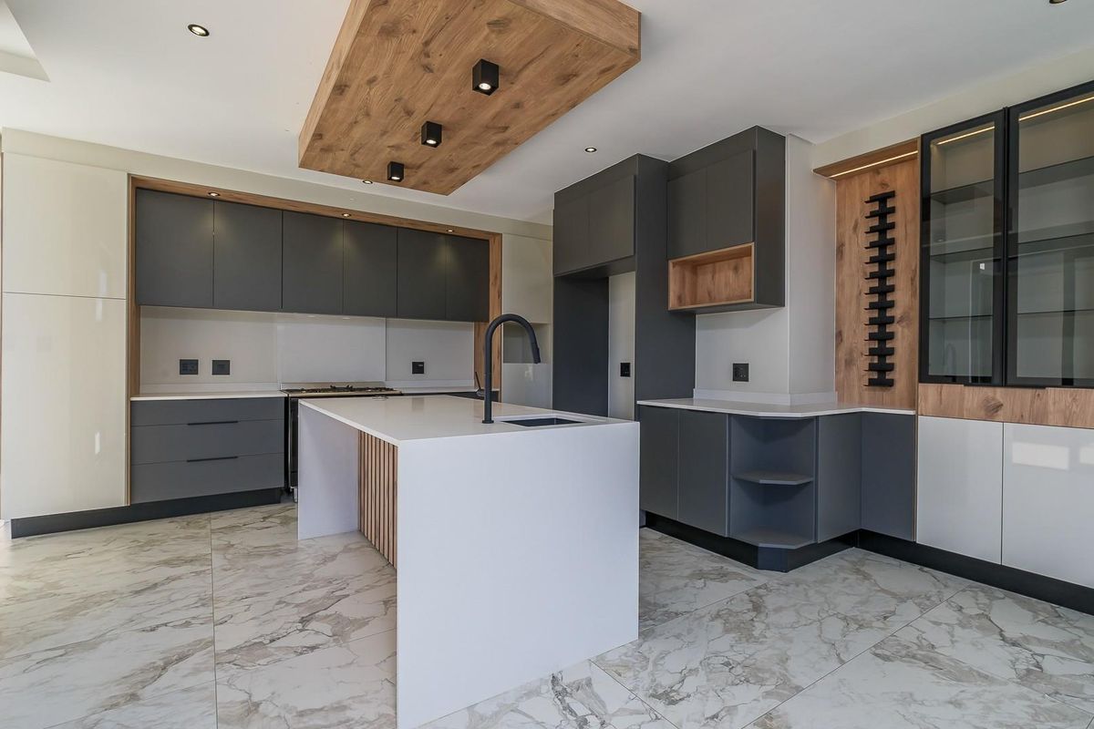 Modern kitchen featuring high-end grey and wood-tone cabinetry, a central island with quartz countertops, marble-look flooring, and integrated lighting features.