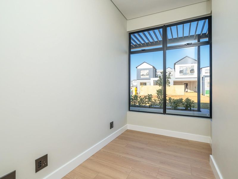 A bright, empty office space featuring modern laminate flooring, clean neutral walls, and a large window providing natural light and a view of the neighborhood.
