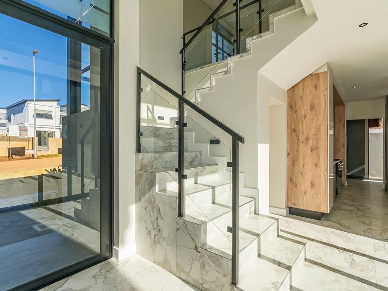 Modern entrance hall featuring a striking marble-look staircase with glass balustrades, large format floor tiles, and seamless access to the open-plan living area.