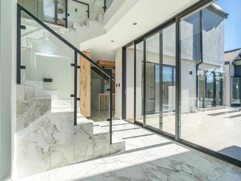 Modern entrance hall featuring a striking marble-clad staircase with glass balustrades and expansive sliding doors opening to the outdoor patio area.