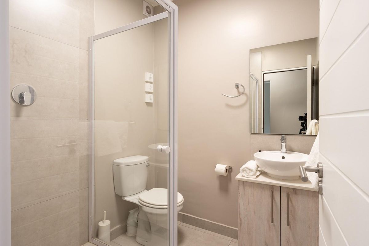 A modern bathroom featuring a glass-enclosed shower, a contemporary vanity with a vessel sink, and neutral wall tiling.