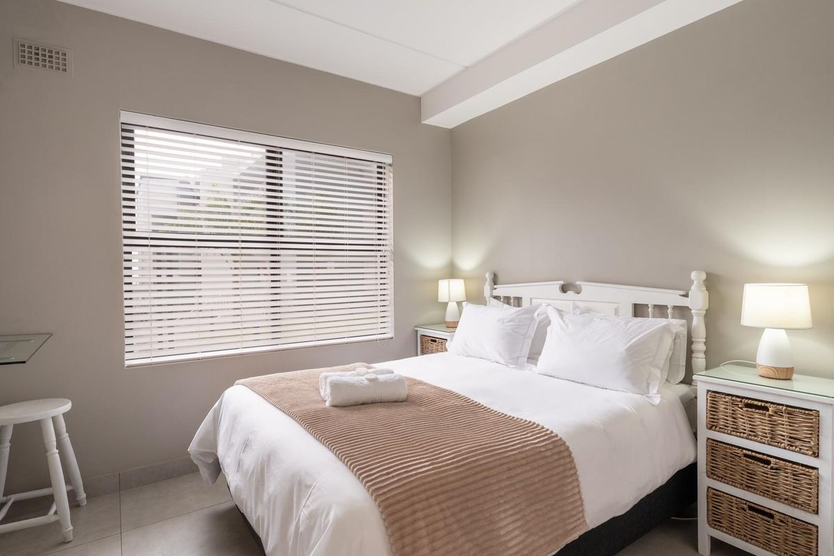 A well-maintained bedroom featuring neutral wall tones, tiled flooring, and a large window fitted with horizontal blinds for natural light control.