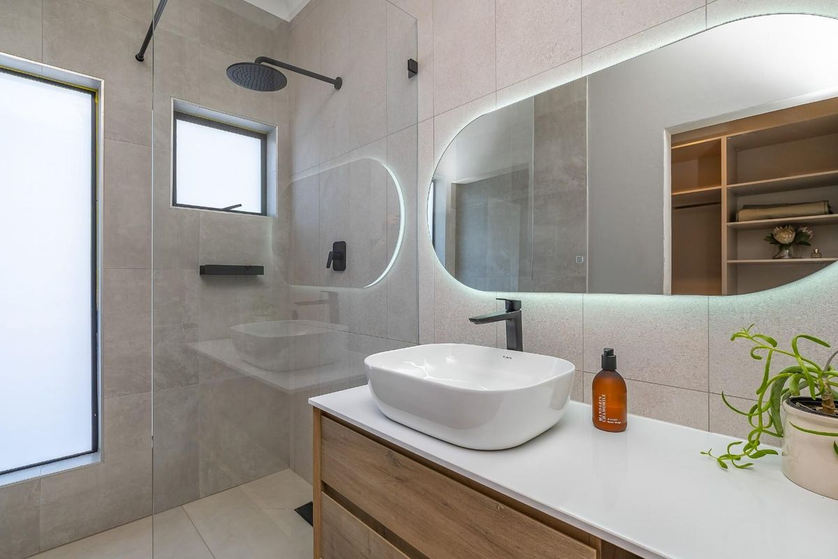 Modern bathroom featuring a floating timber vanity, vessel sink, matte black fixtures, walk-in glass shower, and a backlit oval mirror.