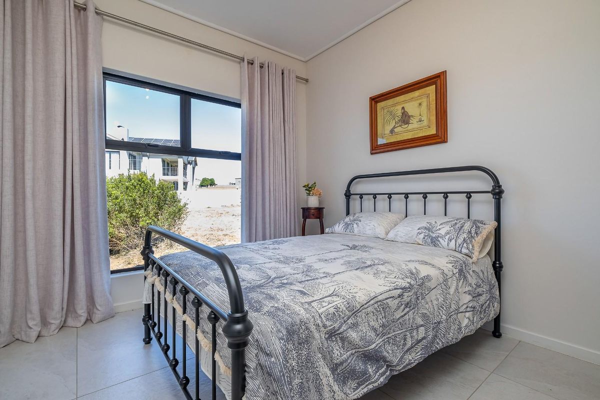 A bright bedroom featuring large windows with curtain tracks and neutral tiled flooring.