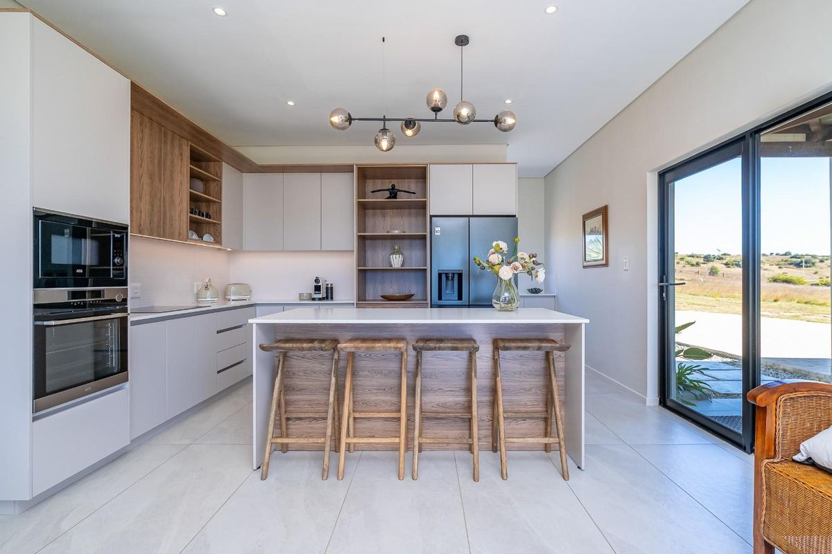 Modern kitchen featuring sleek cabinetry, a central island with breakfast bar seating, integrated appliances, and direct access to the outdoor patio area.