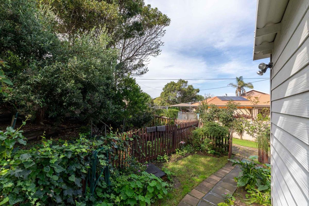 A view of the rear garden featuring a paved pathway, established greenery, and a timber fence alongside the property's weatherboard exterior.