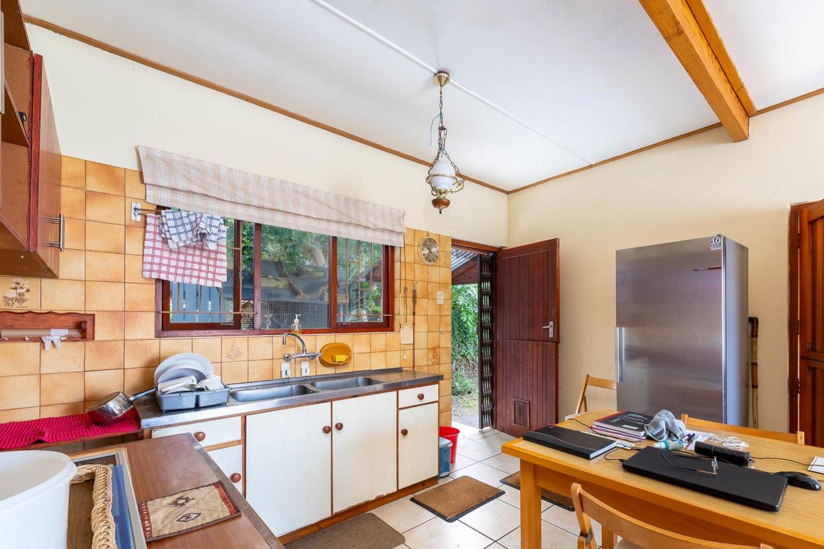 A dated kitchen featuring timber cabinetry, tiled splashbacks, and direct access to the exterior, offering potential for a modern renovation.