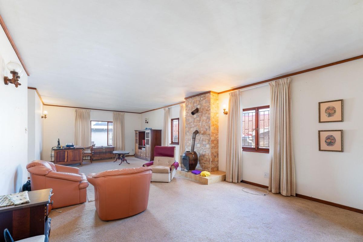 Spacious living room featuring a stone-clad fireplace, carpeted flooring, and large windows with security bars.