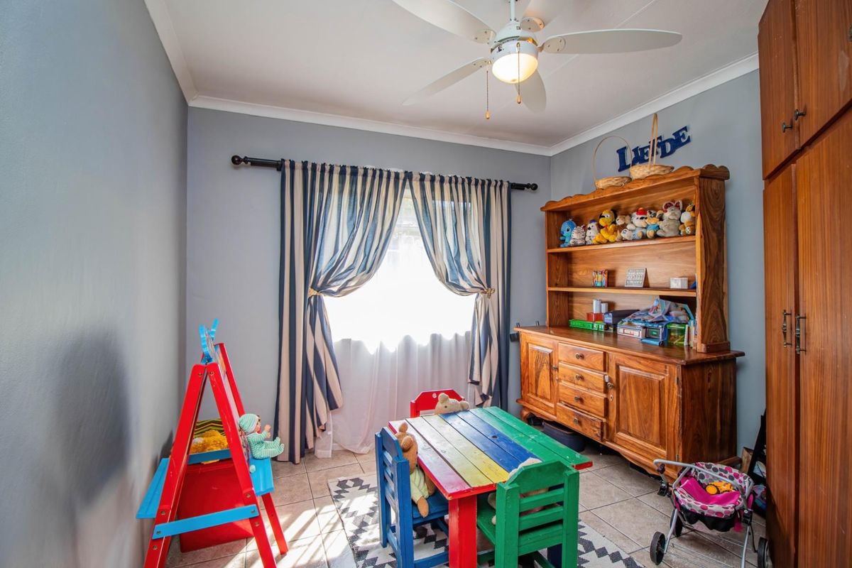 A functional bedroom featuring tiled flooring, a ceiling fan, and built-in wooden cabinetry, currently utilized as a children's play area.