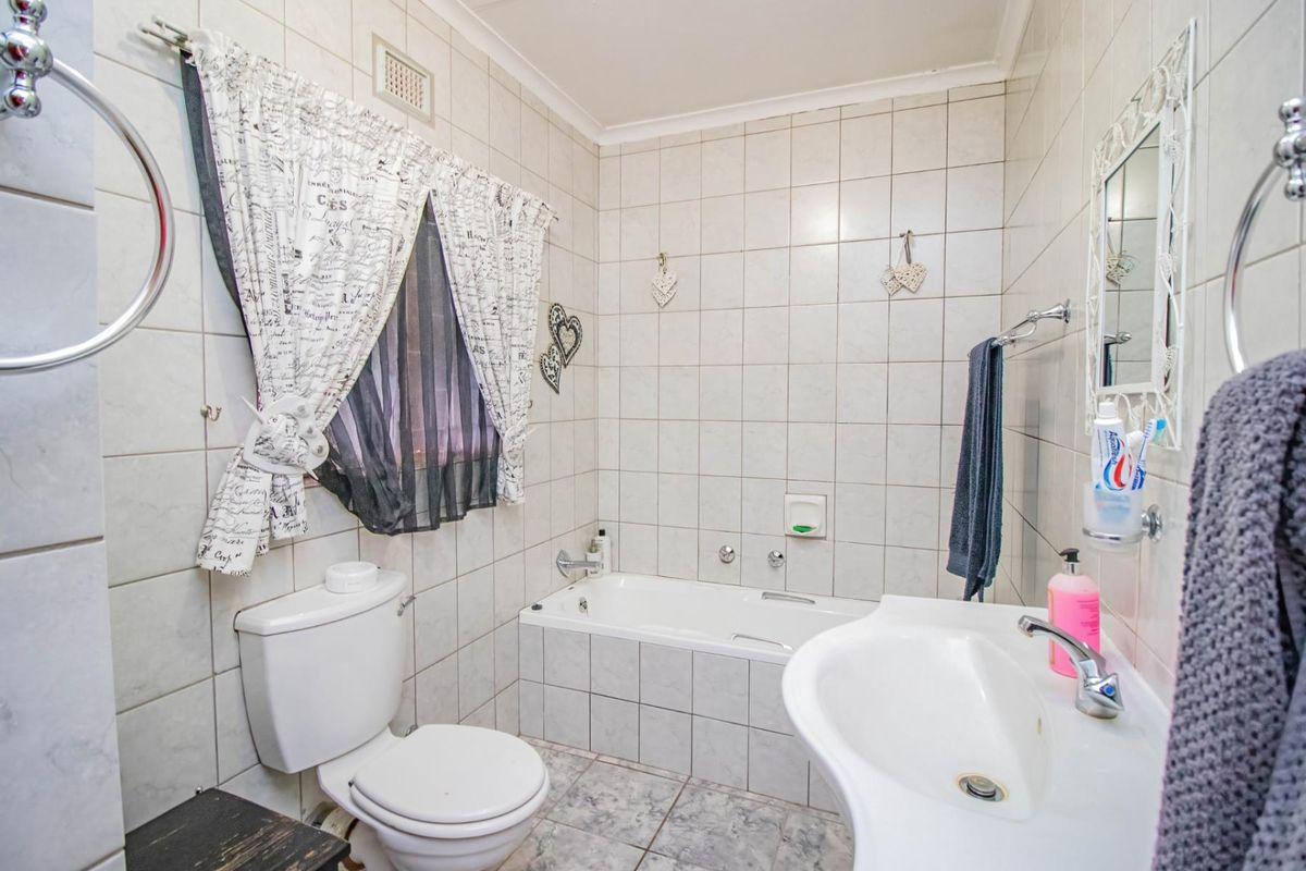 A functional bathroom featuring a built-in bathtub, pedestal sink, and toilet with full-height wall tiling.