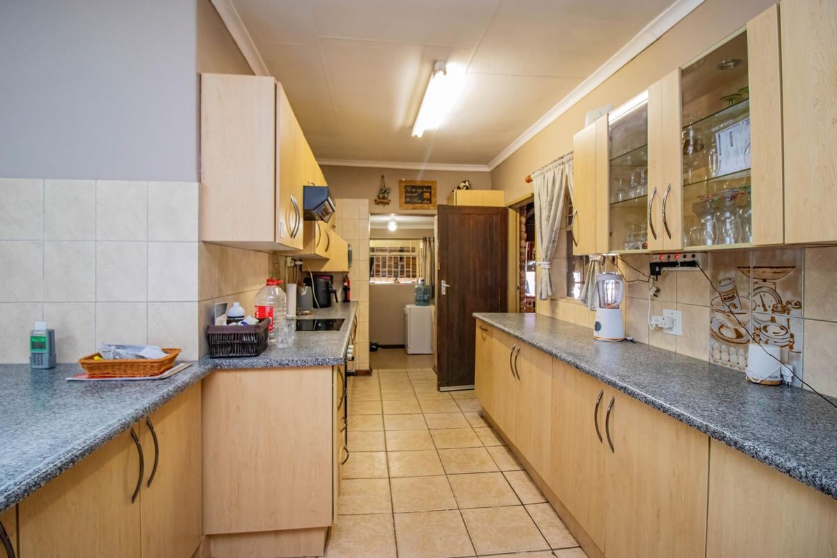 A functional galley-style kitchen featuring light wood cabinetry, granite-look laminate countertops, tiled splashbacks, and ceramic floor tiles.