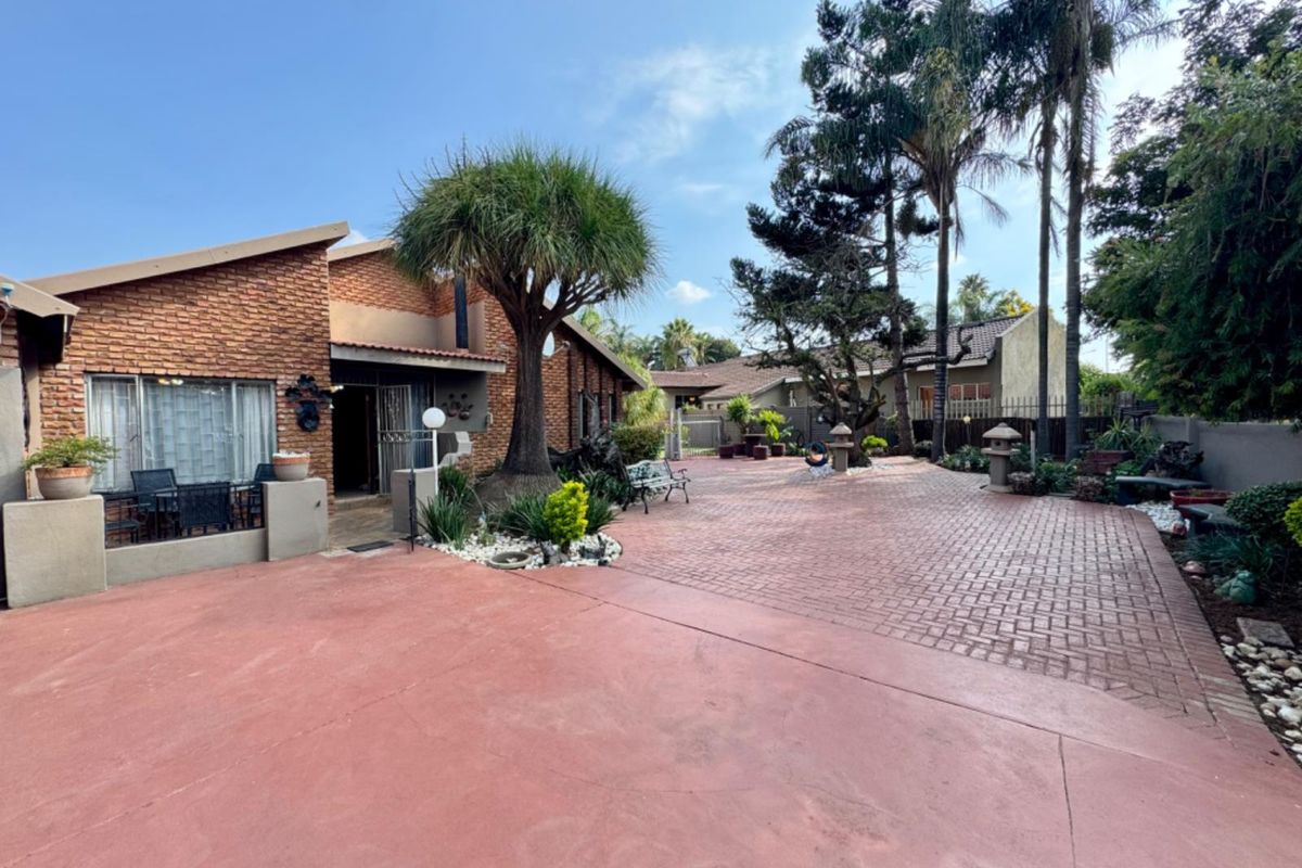 Spacious exterior rear area featuring a large paved courtyard, established trees, and a brick-faced building facade with a covered patio section.