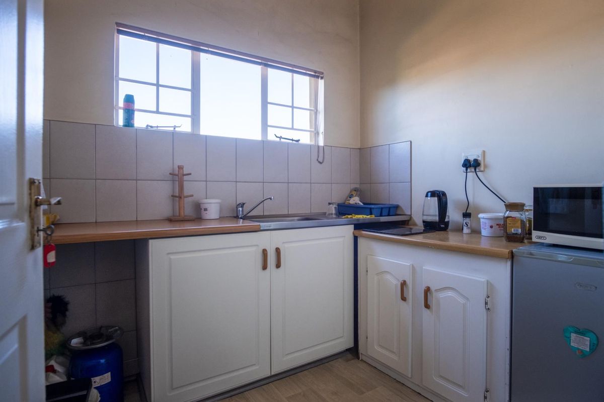 A functional kitchenette featuring built-in white cabinetry, a stainless steel sink, laminate countertops, and a tiled backsplash under a window.