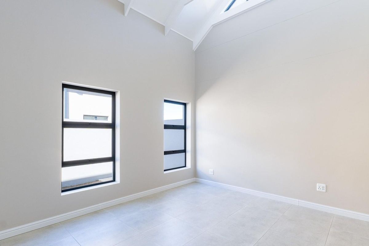 A bright, modern bedroom featuring high vaulted ceilings, neutral tiled flooring, built-in cabinetry, and large windows that provide ample natural light.