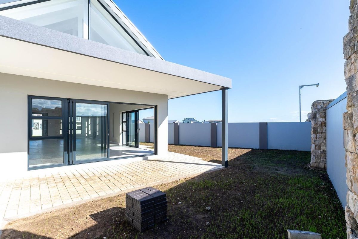 Modern rear exterior featuring a covered patio with large sliding glass doors, stone feature wall, and a spacious backyard area.