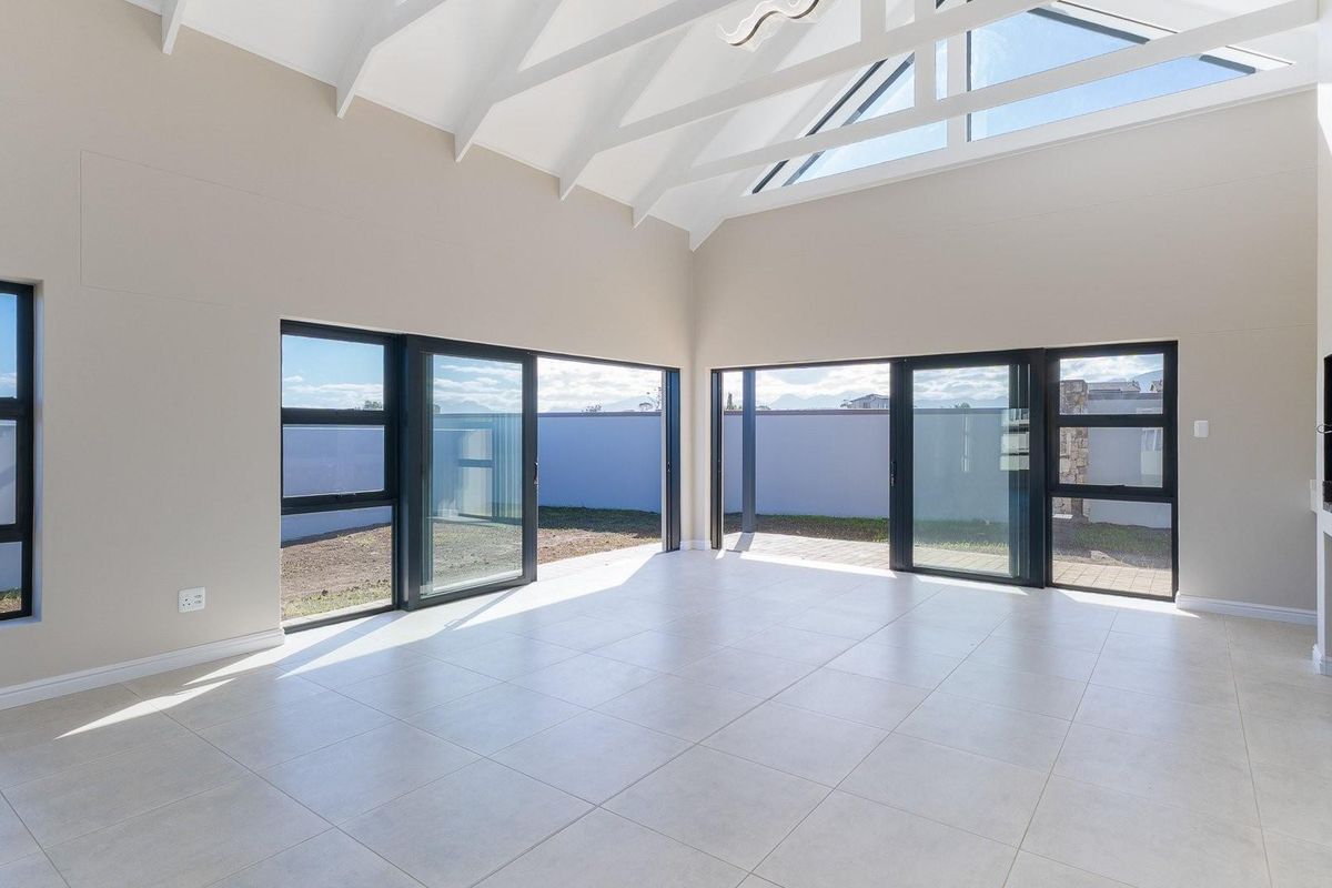 Spacious, light-filled living area featuring high vaulted ceilings with exposed beams, large glass sliding doors, and modern tiled flooring.
