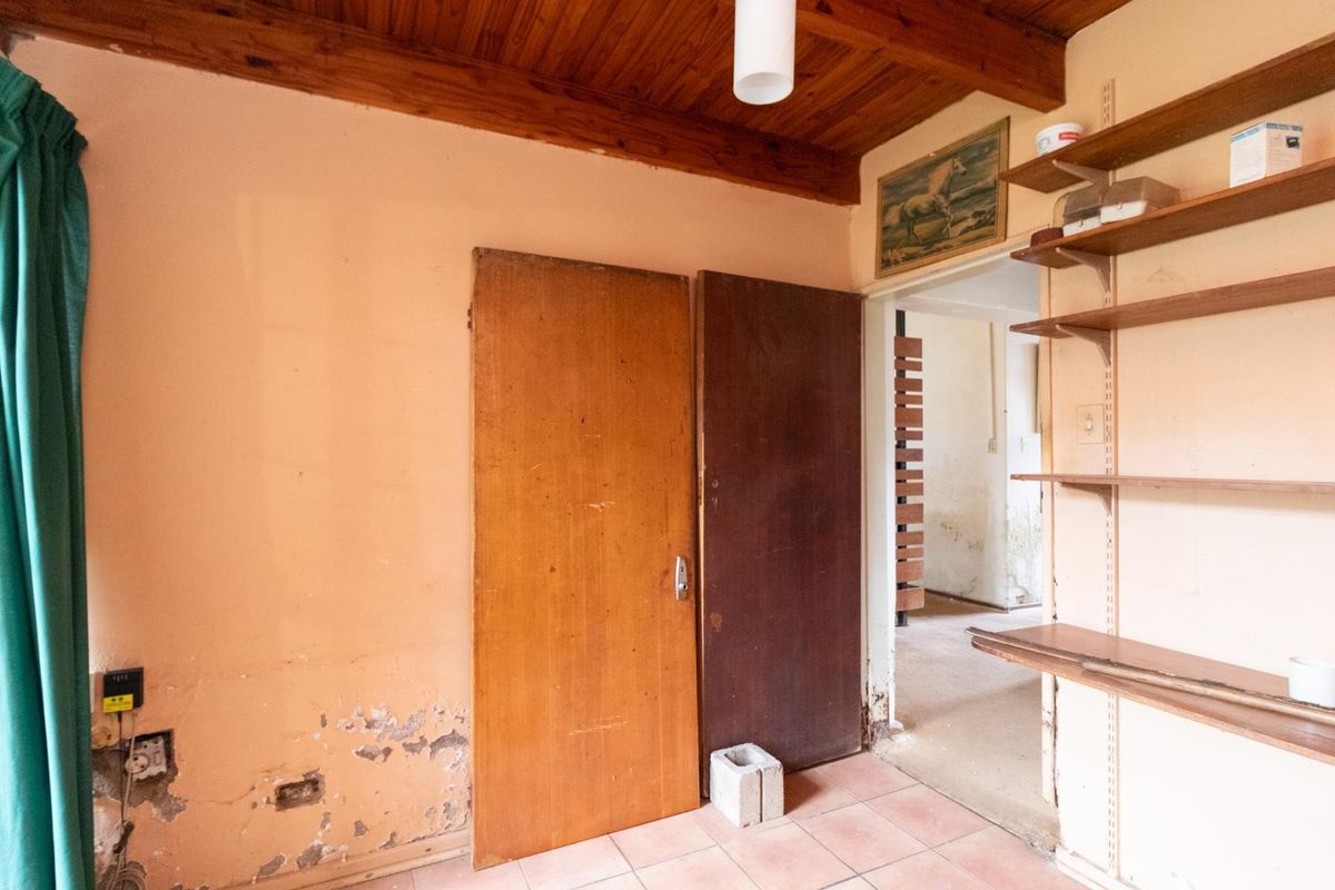 A bedroom or utility space featuring a timber-clad ceiling, tiled flooring, and built-in shelving, currently requiring cosmetic refurbishment and wall repairs.