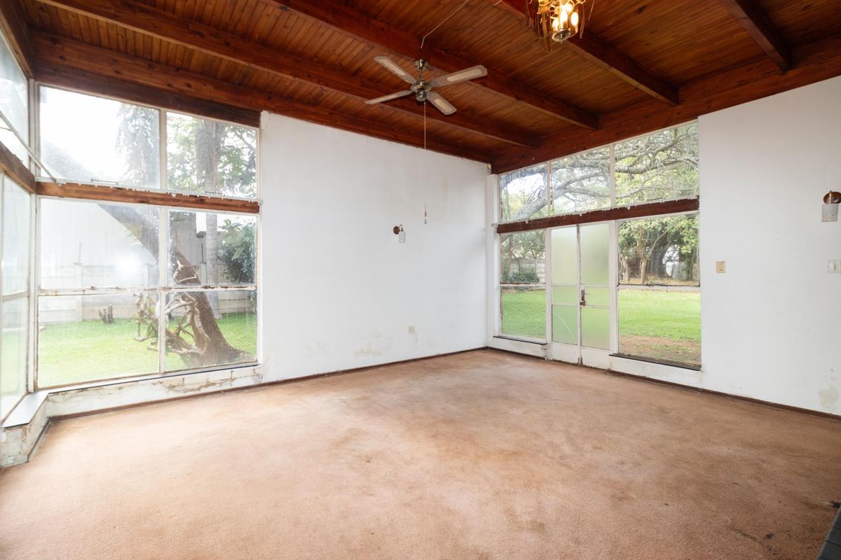 Spacious living area featuring exposed timber beam ceilings, large windows with garden views, and carpeted flooring.