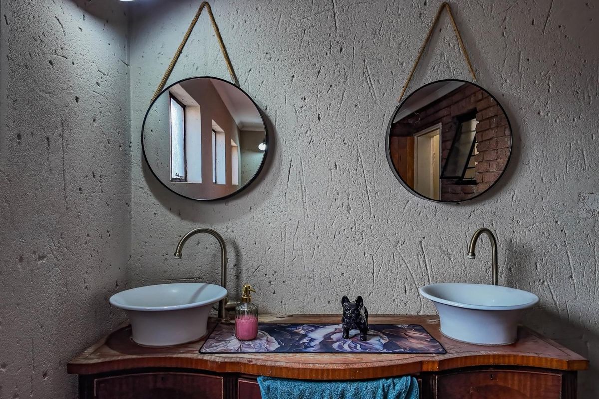 A double vanity bathroom featuring twin vessel sinks with modern brass faucets and circular hanging mirrors against a textured wall finish.