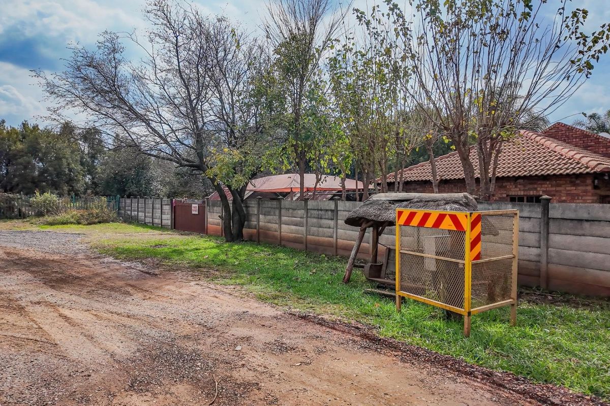 Exterior view of the property boundary featuring a concrete perimeter wall, mature trees, and an unpaved access road.