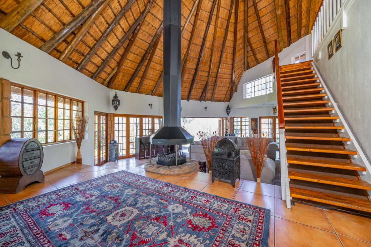 Spacious living area featuring a high thatched ceiling, a central suspended fireplace, tiled flooring, and a wooden staircase leading to the upper level.