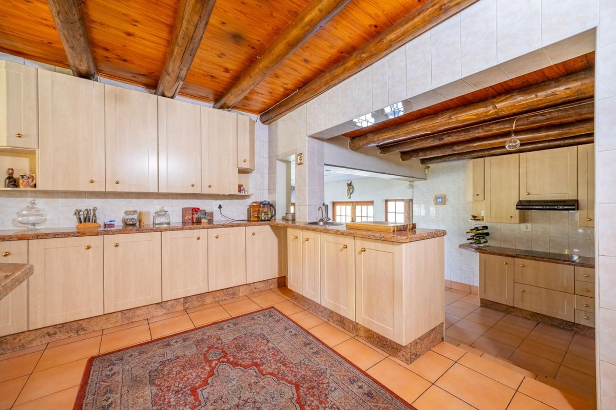 Spacious kitchen featuring light wood cabinetry, granite-look countertops, tiled flooring, and a rustic exposed timber beam ceiling.