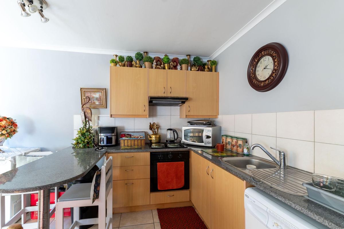 A functional kitchen featuring light wood cabinetry, granite countertops, a built-in oven with extractor fan, and a stainless steel sink with drainer.