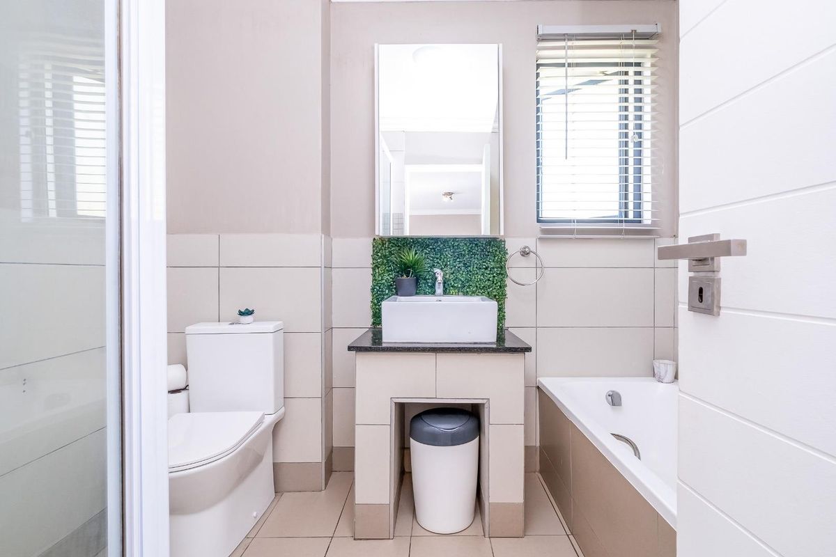A well-maintained bathroom featuring a built-in vanity with a vessel sink, a bathtub, a toilet, and a shower enclosure with neutral tiling.