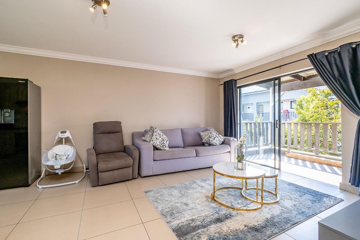 A bright living room featuring large sliding glass doors that open onto a private balcony, finished with neutral floor tiles and crown molding.