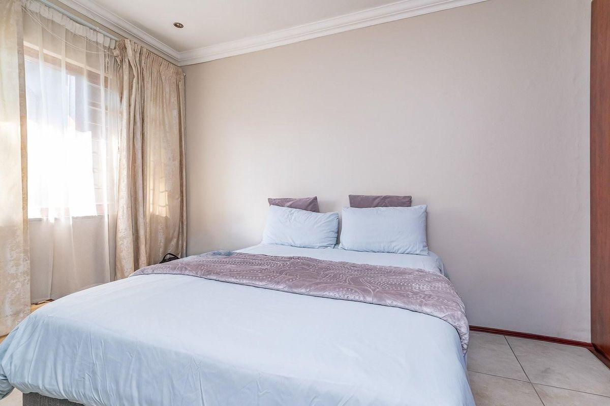 A bedroom featuring tiled flooring, built-in wooden cabinetry, and large windows with curtains, providing a functional and comfortable living space.