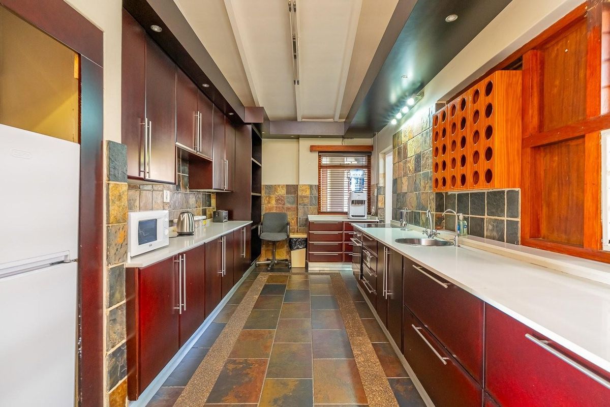 A galley-style kitchen featuring dark wood cabinetry, stone-look tiled flooring, a stone backsplash, and integrated sink fixtures.