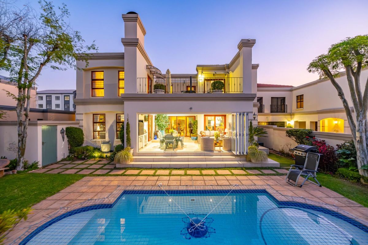 Rear view of a two-story house featuring a swimming pool, paved patio area, and a balcony overlooking the garden.
