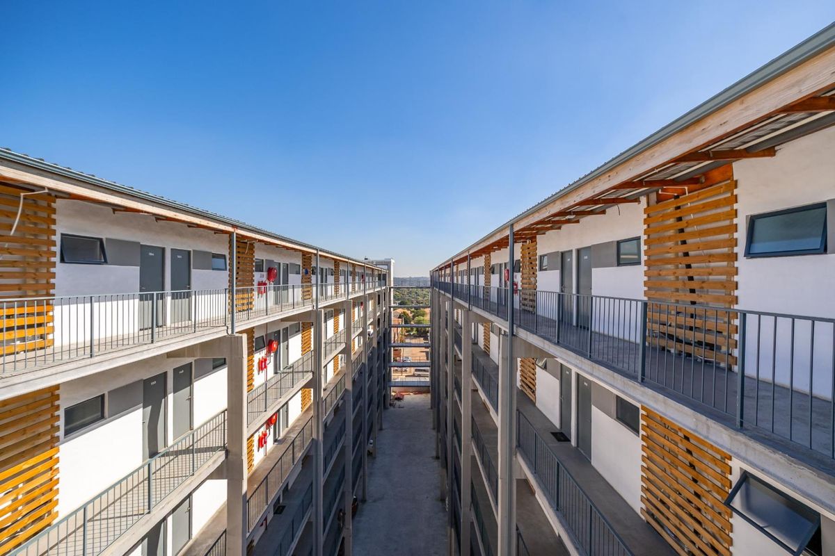 Exterior view of a modern apartment complex featuring multi-level walkways, metal railings, and decorative timber slat facade elements.