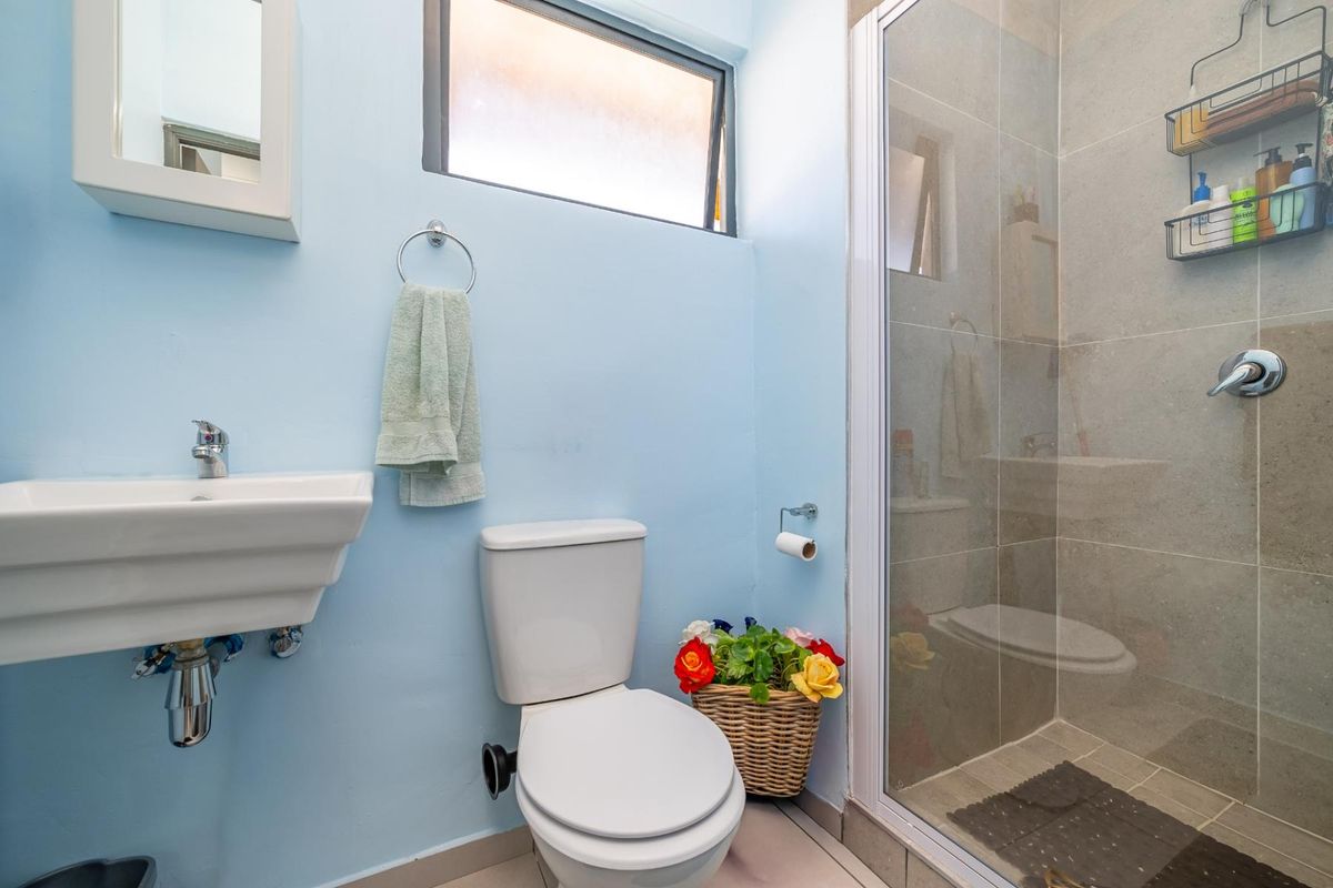 Compact bathroom featuring a wall-mounted basin, a standard toilet, and a tiled shower enclosure with a glass door.