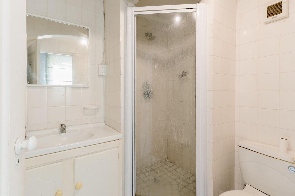 A compact bathroom featuring a white vanity with integrated basin, a corner shower enclosure, and a standard toilet, finished with white wall tiles.