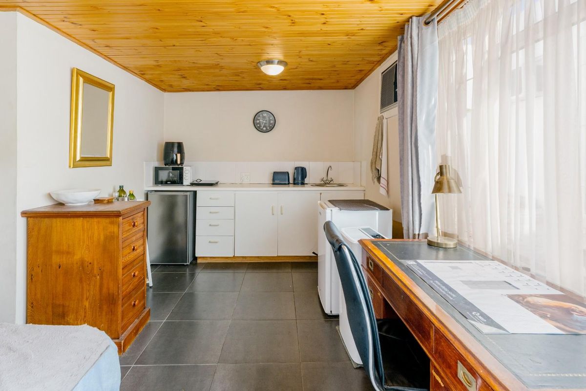 A compact kitchenette area featuring white cabinetry, tiled flooring, and a timber-paneled ceiling, integrated into a multi-purpose living space.