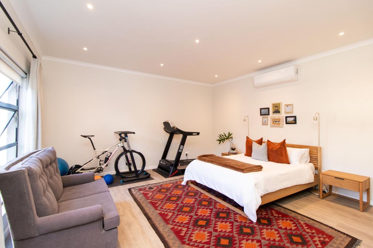 A spacious bedroom featuring recessed lighting, a wall-mounted air conditioning unit, and large windows, currently utilized as a multi-functional living and exercise space.