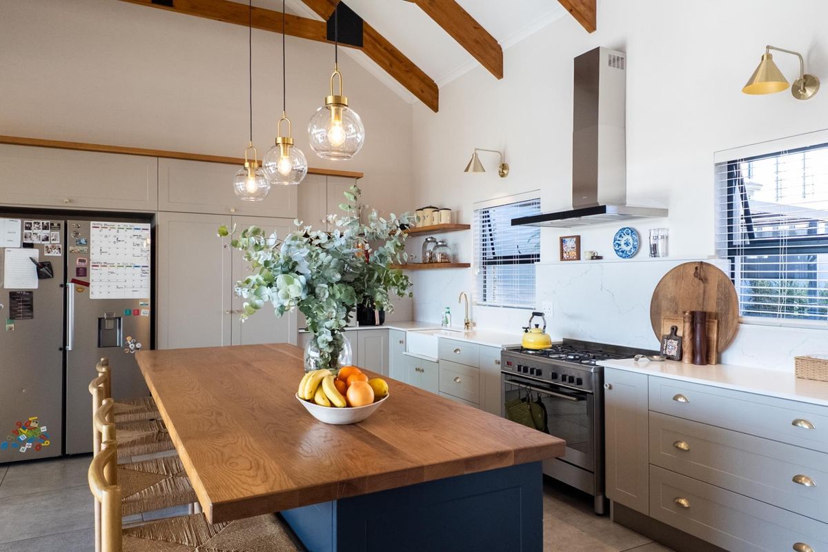 Modern kitchen featuring a large wooden island, farmhouse sink, gas stove with extractor fan, and exposed timber ceiling beams.