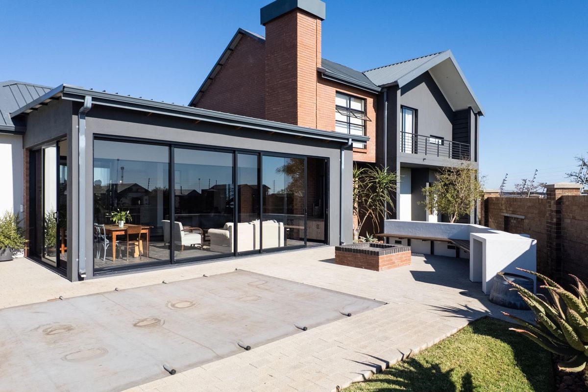 A modern rear exterior view featuring a paved patio, built-in fire pit, integrated seating, and large sliding glass doors leading into the living area.