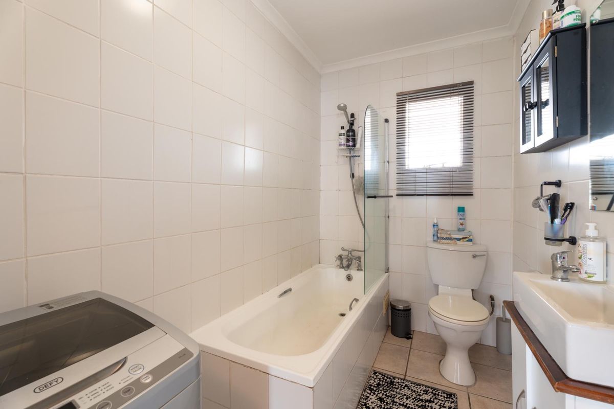 Functional bathroom featuring a bathtub with shower screen, toilet, and washbasin, finished with white wall tiles and neutral floor tiles.