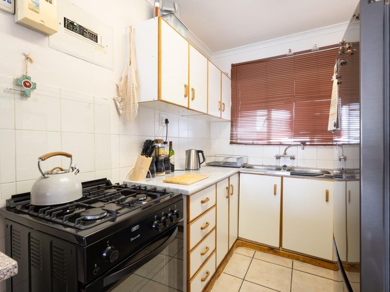 Compact kitchen featuring white cabinetry, gas stove with oven, tiled backsplash, and double basin sink with functional layout.