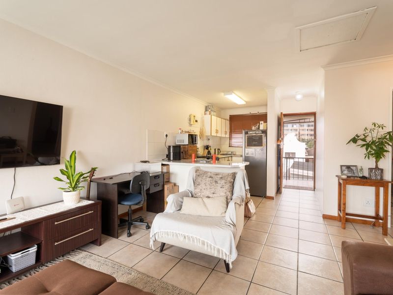 Open-plan living area featuring tiled flooring, a functional kitchen space with cabinetry, and direct access to an exterior balcony.