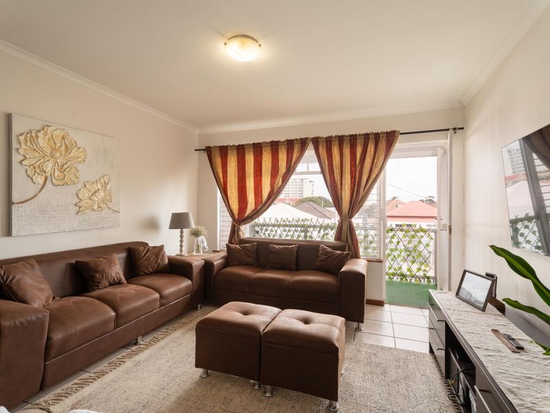 A well-lit living room featuring tiled flooring, coving, and direct access to a private balcony through a glass-paneled door.