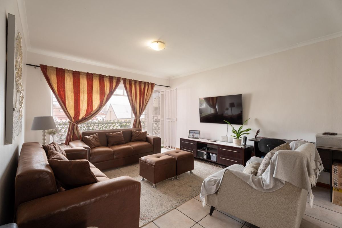 A comfortable living room featuring tiled flooring and direct access to a balcony through a sliding door with an integrated security gate.