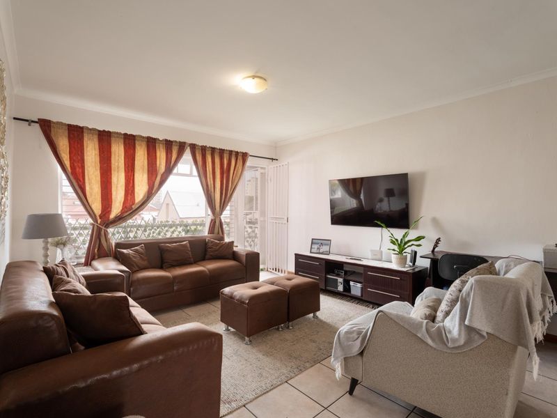 A comfortable living room featuring tiled flooring and direct access to a balcony through a sliding door with an integrated security gate.