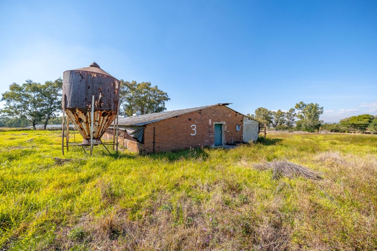 A rustic farm outbuilding featuring exposed brick construction and an adjacent metal silo, situated on a large open field.