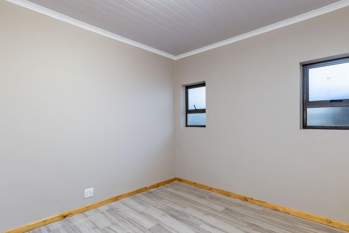 A clean, empty bedroom featuring neutral wall tones, wood-look laminate flooring, timber skirting boards, and two small windows.